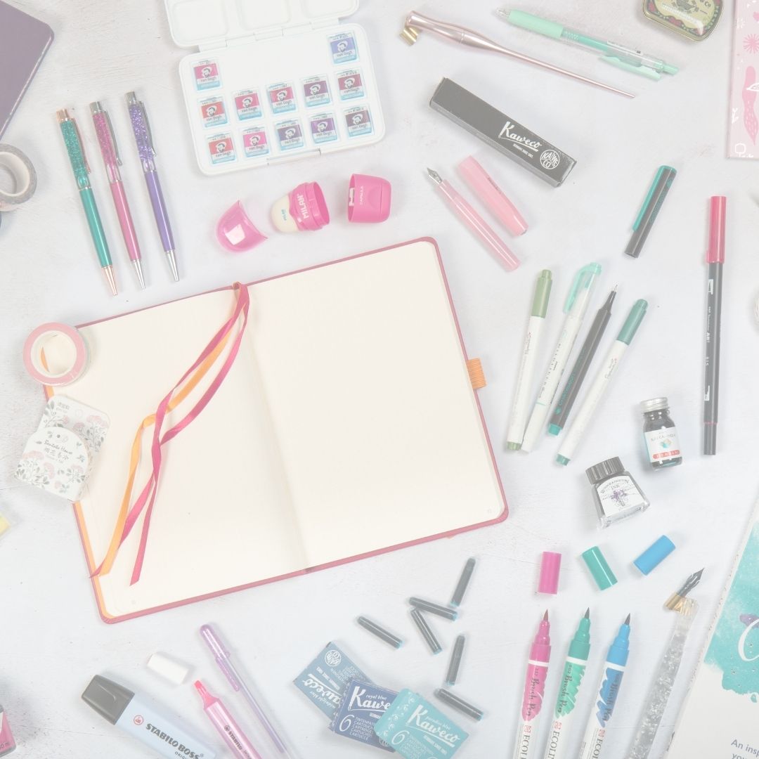 Stationery items including pens, markers, and a notebook on a white surface.