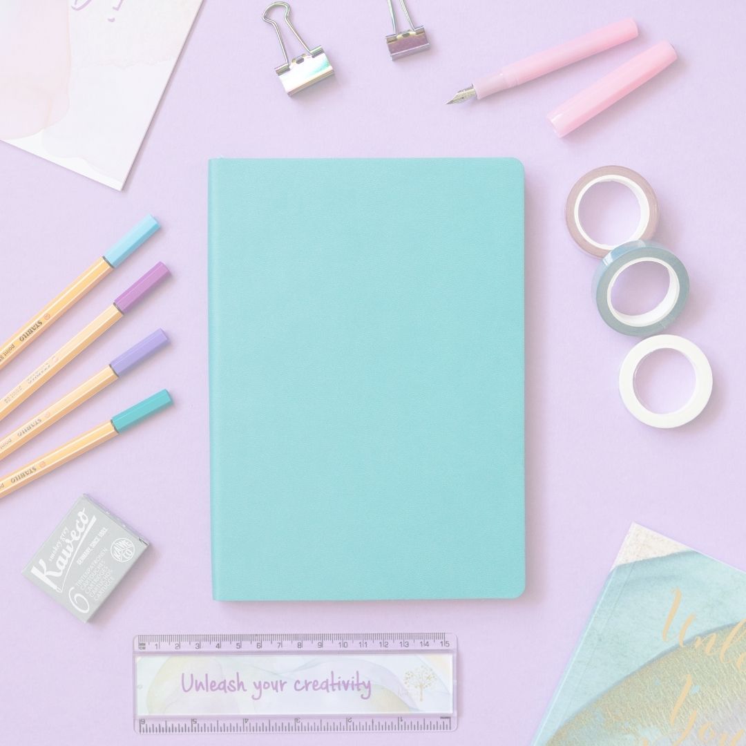 Turquoise notebook surrounded by stationery items on a pink background