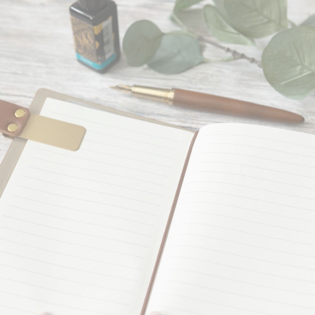 Notebook with pen and leaves on a light surface