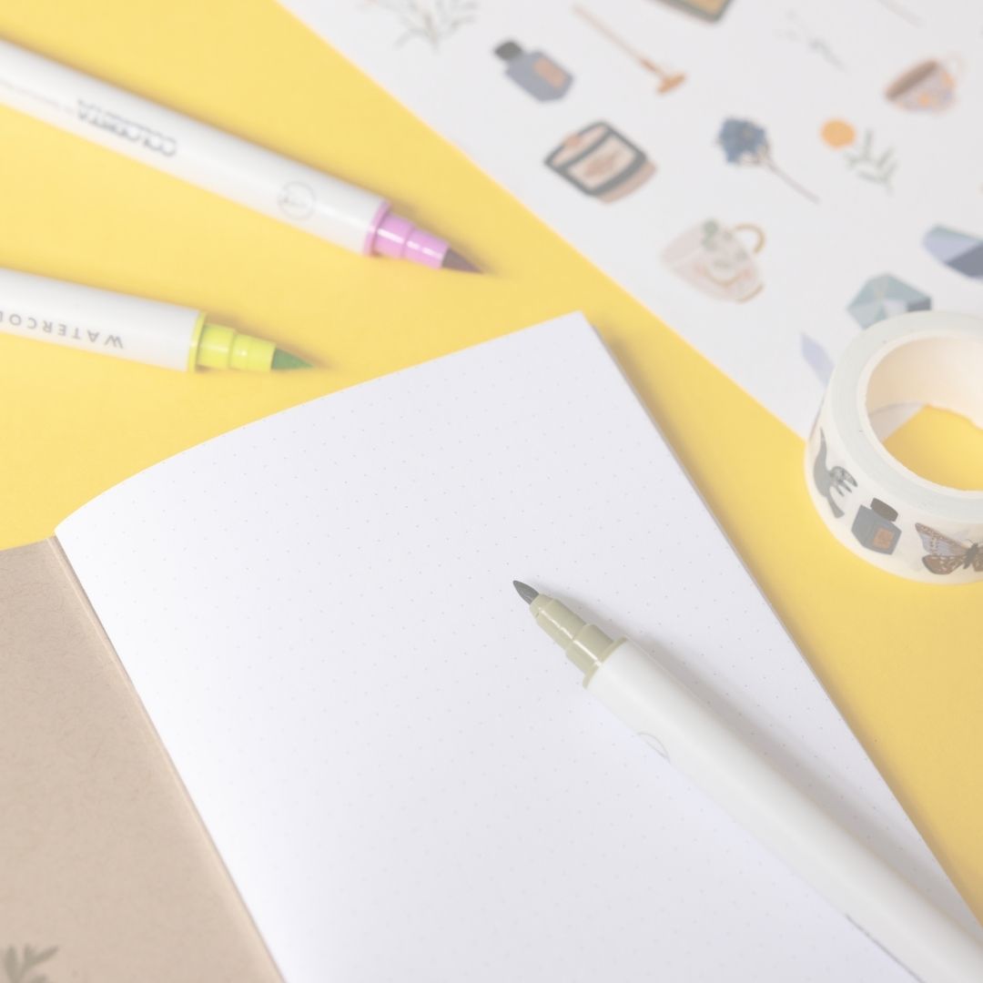 Stationery items including a pen, markers, and washi tape on a white surface with a yellow border.