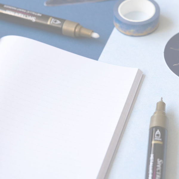 White notebook with a pen and tape on a light blue surface