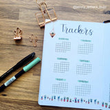 Tracker sheet with various activities in a dot grid bullet journal on a wooden surface with stationery items.