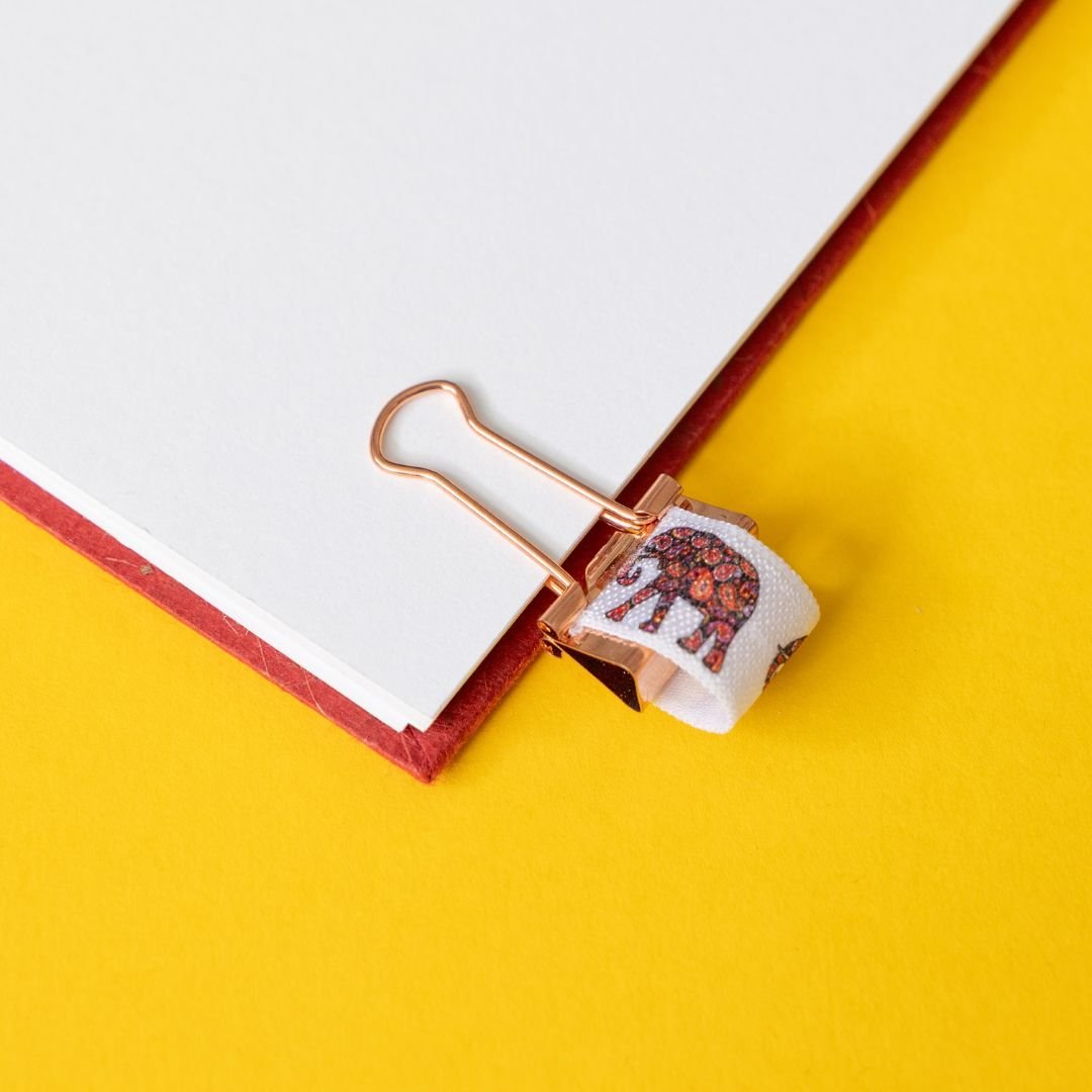 Rose gold binder clip with elephant elastic on an open book against a yellow background