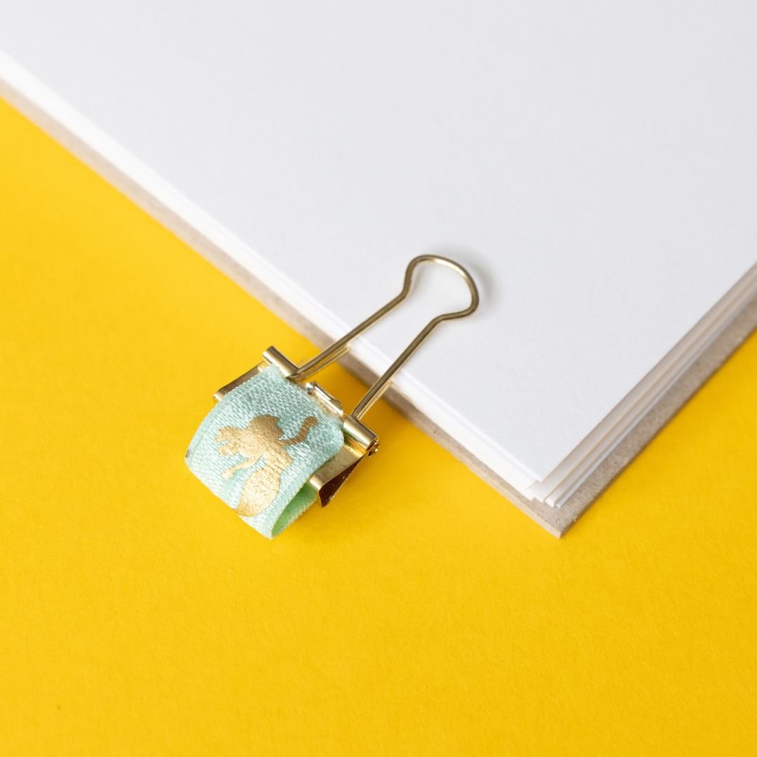 Decorative mermaid pen clip with gold accents on a yellow background
